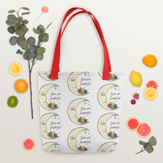 A white tote bag with a printed design featuring a crescent moon, stars, and the text 'You are powerful'. The bag has dual red handles. affirmation canvas tote bag minimal design, ADHD supportive reminder tote, inspirational everyday tote bag